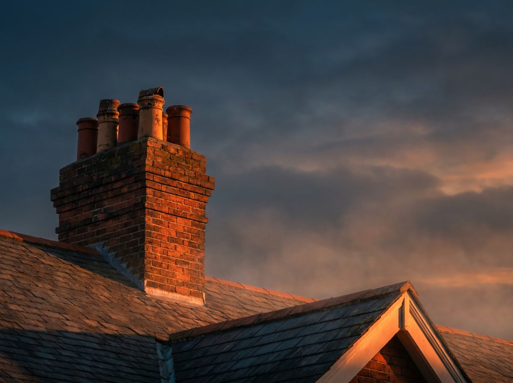 A Dayton Chimney Co. sweep on the roof of a brick home at dusk
